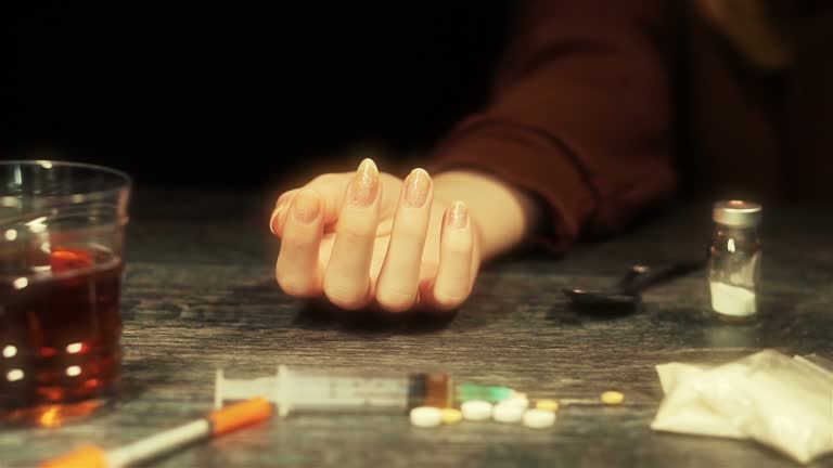A woman dying from excessive alcohol use and syringe, pills, drugs.
